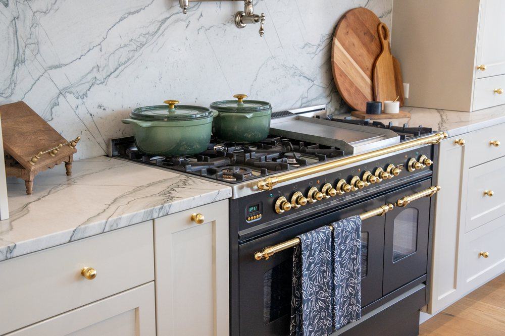 A range top styled with cookware and a marble backsplash