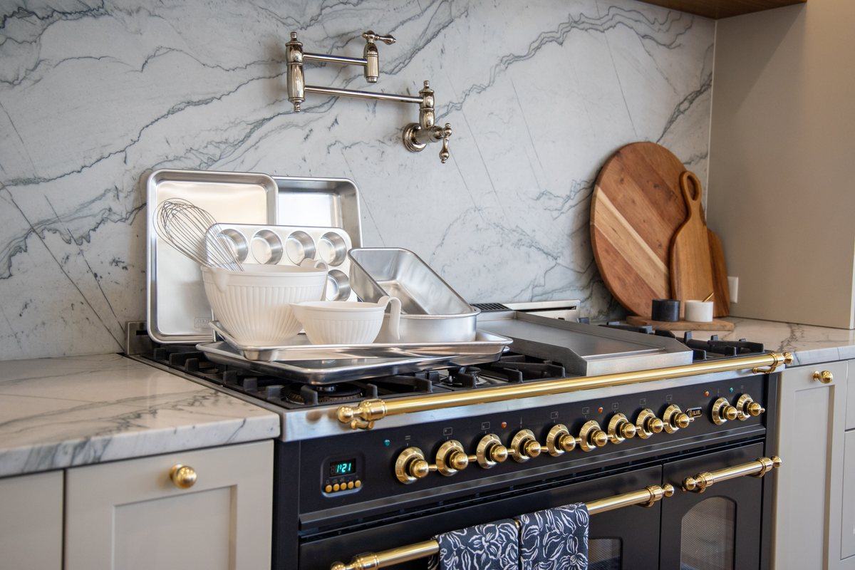 A baking station styled with mixing bowls, sheet pans, and a whisk on a range